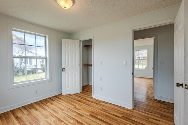 unfurnished bedroom featuring crown molding, a walk in closet, a textured ceiling, and light wood-type flooring