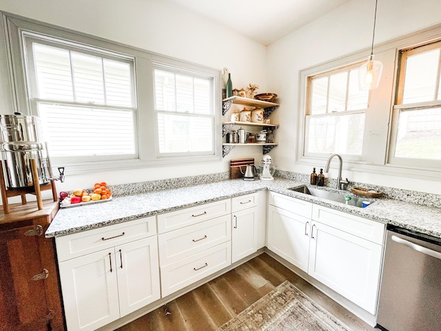 kitchen with hanging light fixtures, light stone countertops, stainless steel dishwasher, white cabinetry, and a sink