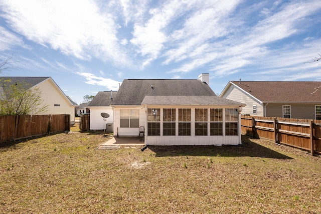 rear view of house with a chimney, a fenced backyard, and a lawn