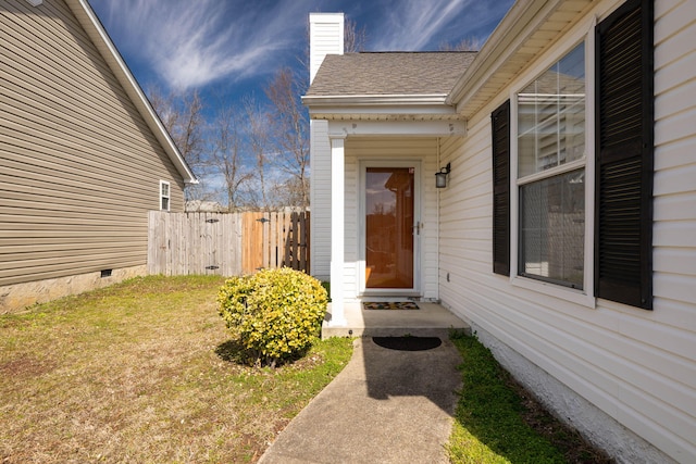 view of exterior entry featuring a shingled roof, a lawn, a chimney, crawl space, and fence