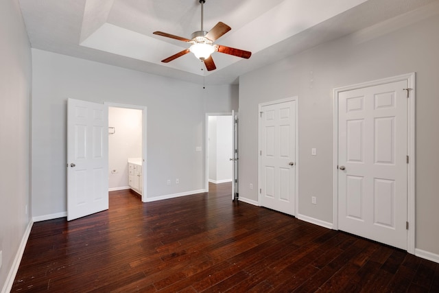 unfurnished bedroom featuring dark wood-type flooring, a raised ceiling, connected bathroom, and baseboards