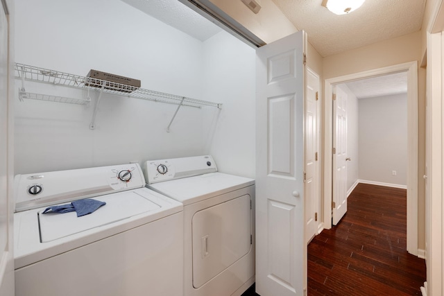 clothes washing area with a textured ceiling, laundry area, dark wood-type flooring, baseboards, and washer and clothes dryer