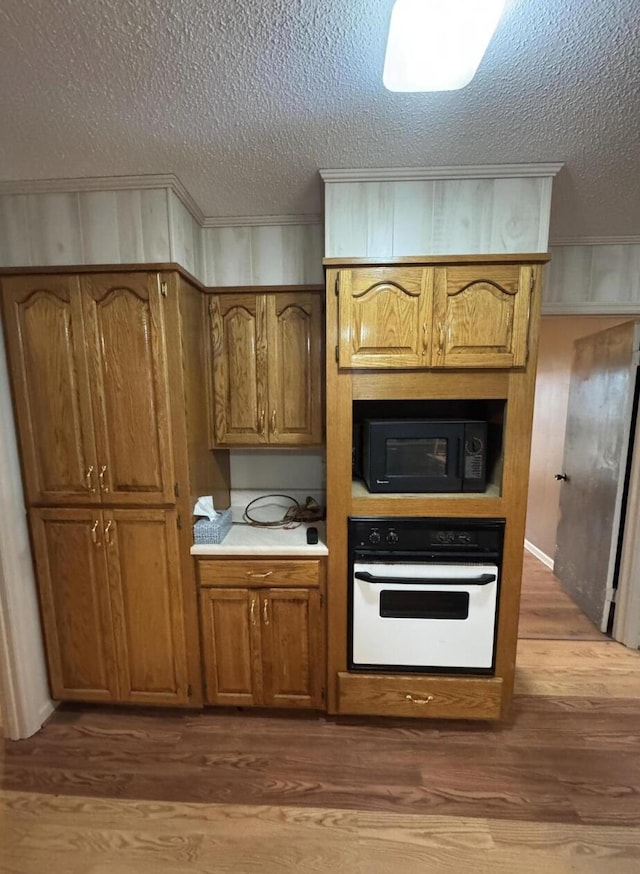 kitchen with wood-type flooring, oven, and a textured ceiling