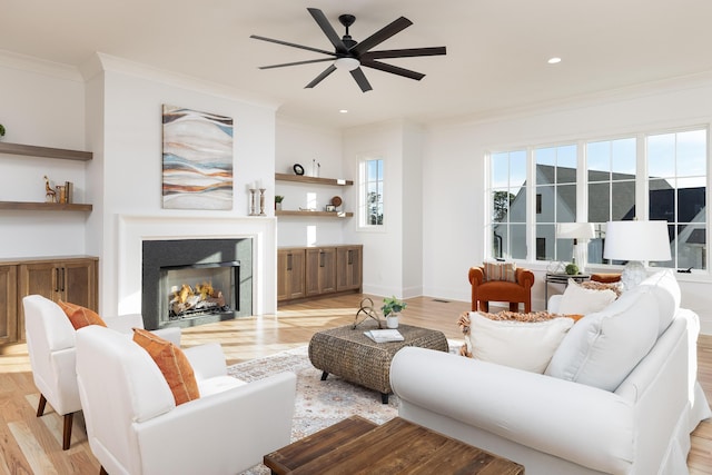 living area featuring a lit fireplace, ornamental molding, light wood-style flooring, and baseboards