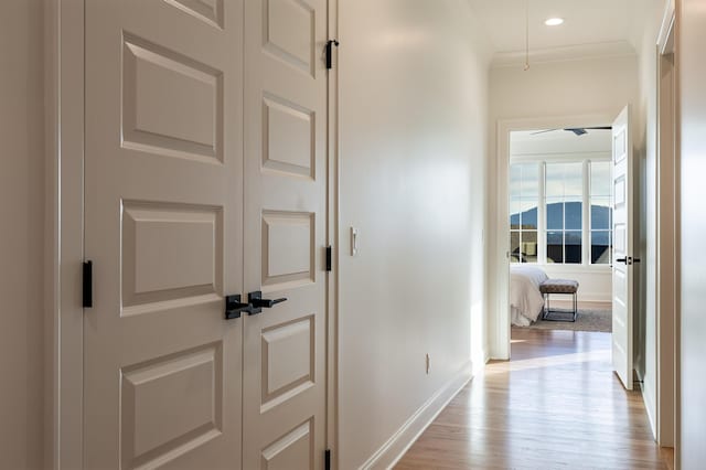 hall featuring light wood-style floors, baseboards, crown molding, and recessed lighting