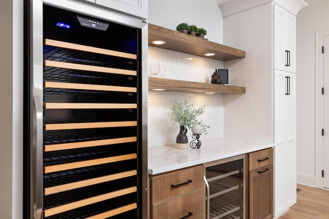 bar featuring light wood-type flooring, wine cooler, and backsplash