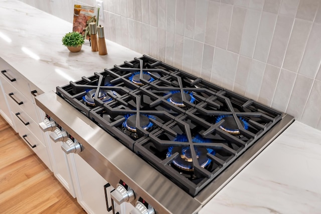 interior details with cooktop, light stone countertops, white cabinetry, and decorative backsplash