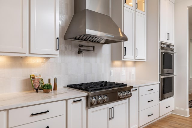 kitchen featuring island range hood, white cabinets, glass insert cabinets, appliances with stainless steel finishes, and light stone countertops