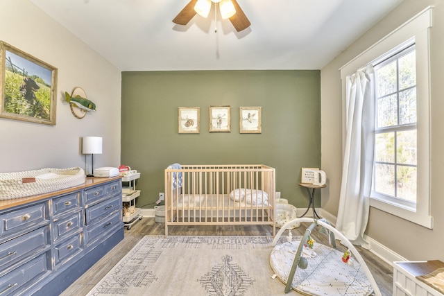 bedroom featuring a nursery area, dark wood-type flooring, and ceiling fan