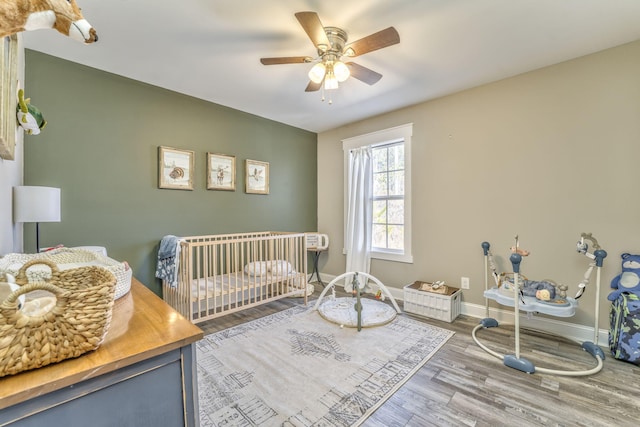 bedroom featuring a nursery area, hardwood / wood-style floors, and ceiling fan