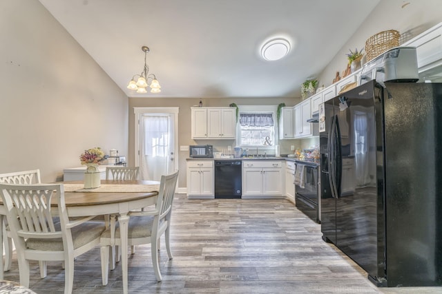 kitchen with lofted ceiling, white cabinets, hanging light fixtures, black appliances, and light hardwood / wood-style flooring