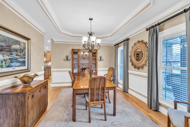 dining area with a notable chandelier, a raised ceiling, light wood-type flooring, and a wealth of natural light