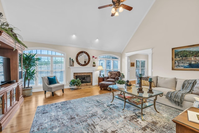 living room with high vaulted ceiling, crown molding, ceiling fan, light hardwood / wood-style floors, and a premium fireplace