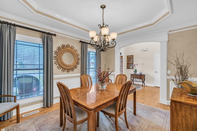 dining area featuring a raised ceiling, a notable chandelier, light wood-type flooring, and ornate columns