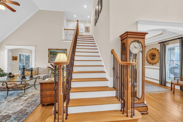 stairs featuring hardwood / wood-style floors, crown molding, high vaulted ceiling, and ceiling fan