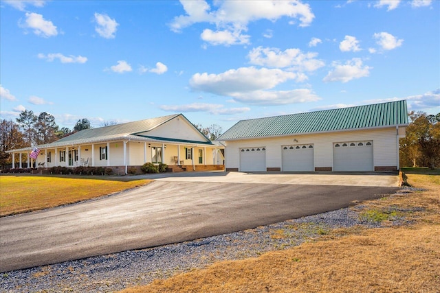 view of front facade featuring a detached garage, covered porch, metal roof, an outdoor structure, and a front lawn