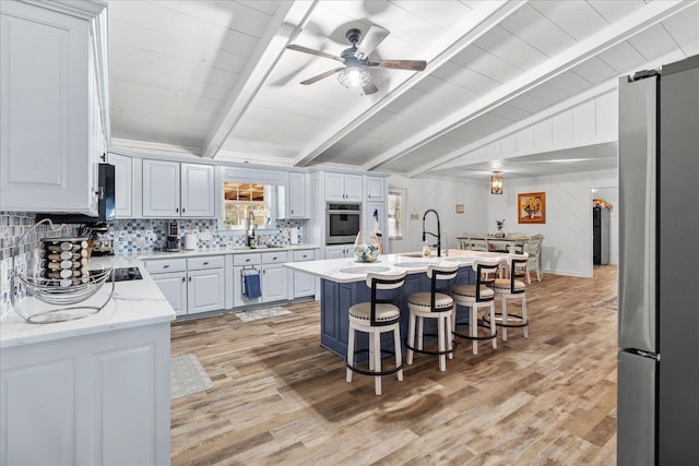 kitchen featuring a breakfast bar, vaulted ceiling with beams, light wood finished floors, stainless steel appliances, and tasteful backsplash