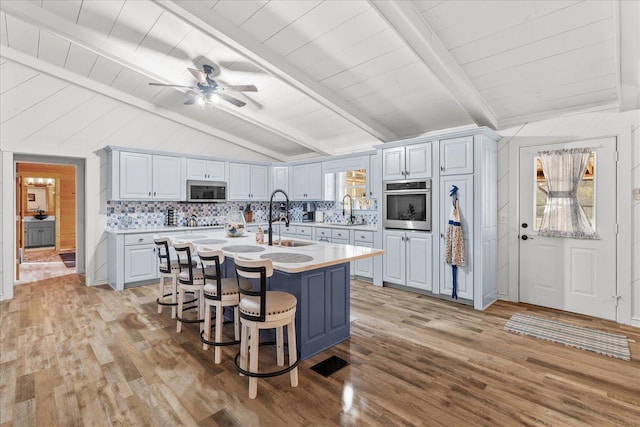 kitchen featuring stainless steel appliances, light countertops, a sink, and lofted ceiling with beams