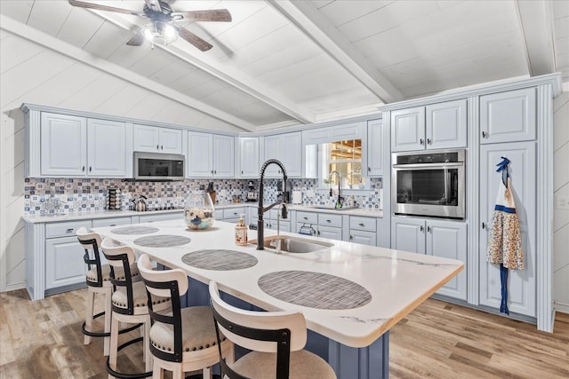 kitchen with vaulted ceiling with beams, stainless steel appliances, a sink, and light countertops