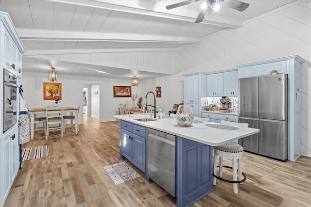 kitchen featuring lofted ceiling with beams, stainless steel appliances, light countertops, blue cabinetry, and light wood finished floors