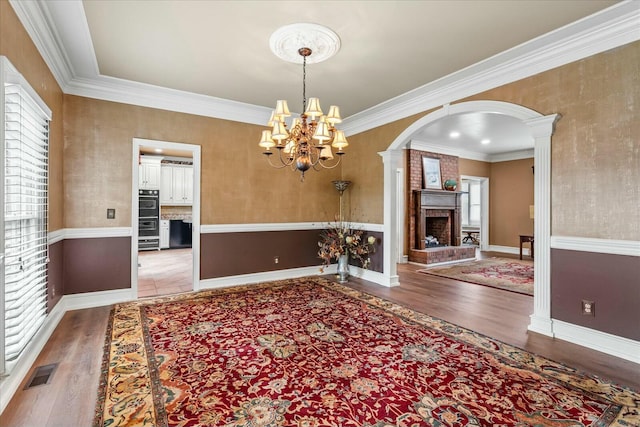 interior space with decorative columns, crown molding, a notable chandelier, a fireplace, and hardwood / wood-style floors