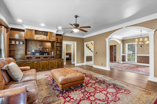 living room with ceiling fan with notable chandelier, wood-type flooring, ornamental molding, and ornate columns