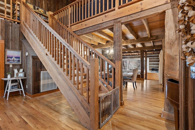 stairway with beam ceiling, a high ceiling, wooden ceiling, wood-type flooring, and wooden walls