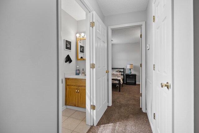 corridor with light tile patterned flooring, light colored carpet, baseboards, and a textured ceiling