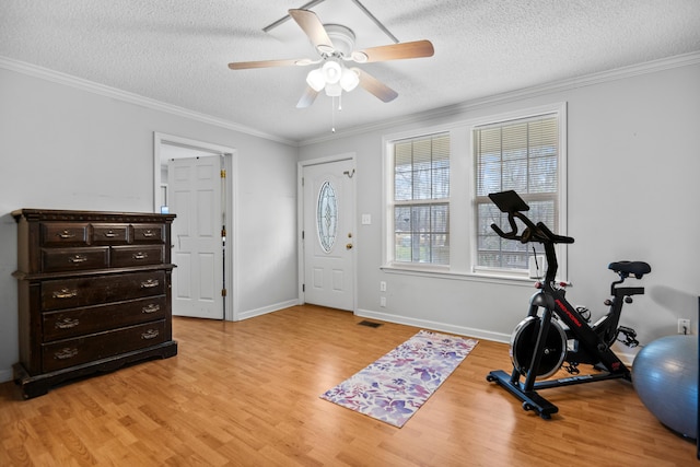 exercise area featuring baseboards, ornamental molding, light wood-style floors, a textured ceiling, and a ceiling fan