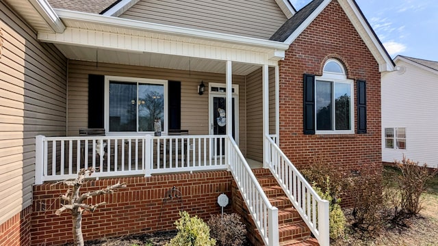 view of exterior entry featuring brick siding, covered porch, and a shingled roof