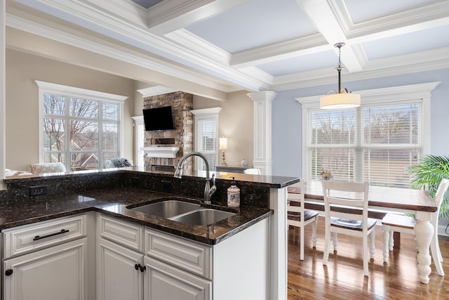 kitchen featuring decorative columns, sink, dark stone countertops, white cabinets, and hanging light fixtures