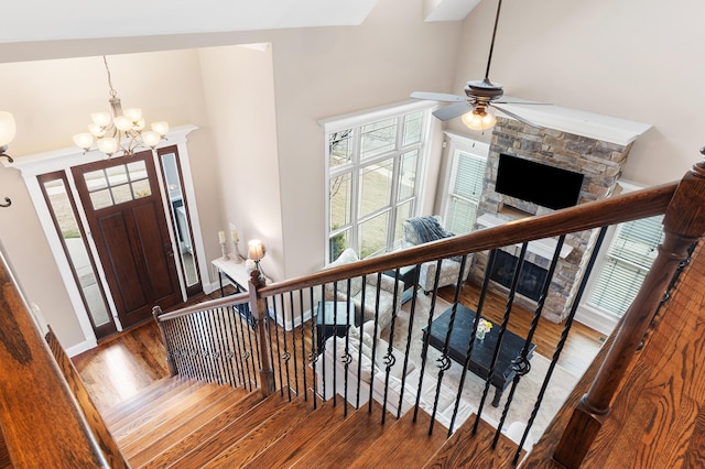 entryway with dark hardwood / wood-style flooring, ceiling fan with notable chandelier, a stone fireplace, and a high ceiling