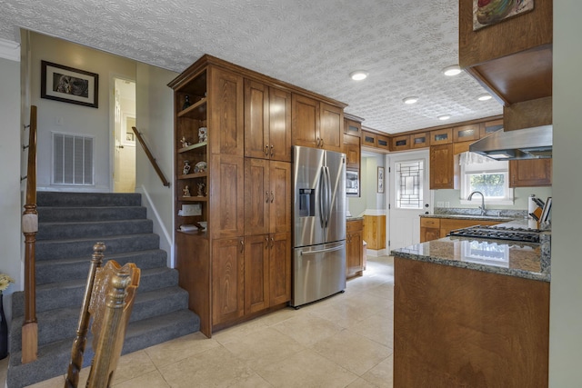 kitchen featuring light tile patterned flooring, ventilation hood, a textured ceiling, appliances with stainless steel finishes, and dark stone counters