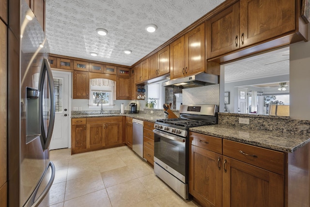 kitchen featuring sink, dark stone counters, light tile patterned floors, stainless steel appliances, and a textured ceiling