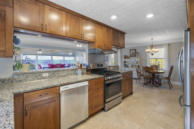 kitchen with light stone counters, ornamental molding, pendant lighting, stainless steel appliances, and ceiling fan with notable chandelier