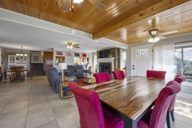 tiled dining area featuring a brick fireplace, ceiling fan with notable chandelier, and wood ceiling