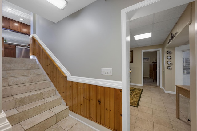 staircase featuring tile patterned flooring, a drop ceiling, and wooden walls