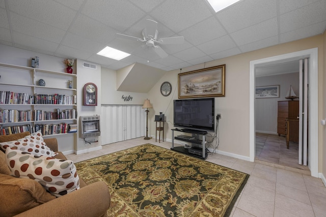 tiled living room with ceiling fan, a paneled ceiling, and heating unit