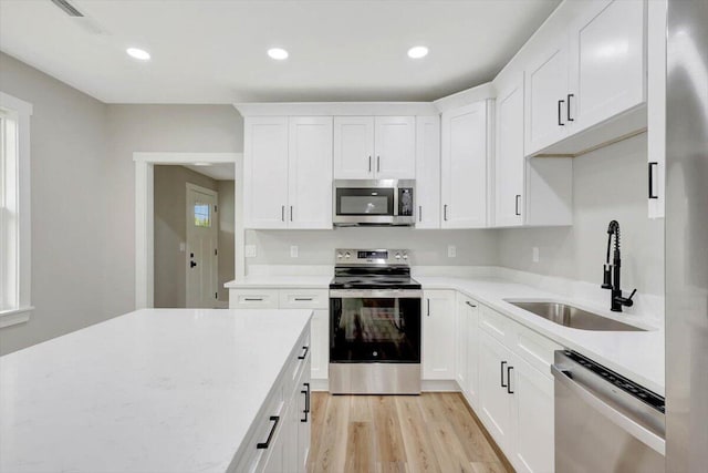 kitchen with a sink, stainless steel appliances, light wood finished floors, light countertops, and white cabinetry