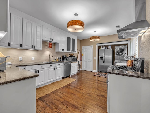 kitchen featuring white cabinetry, stacked washing maching and dryer, ventilation hood, and appliances with stainless steel finishes