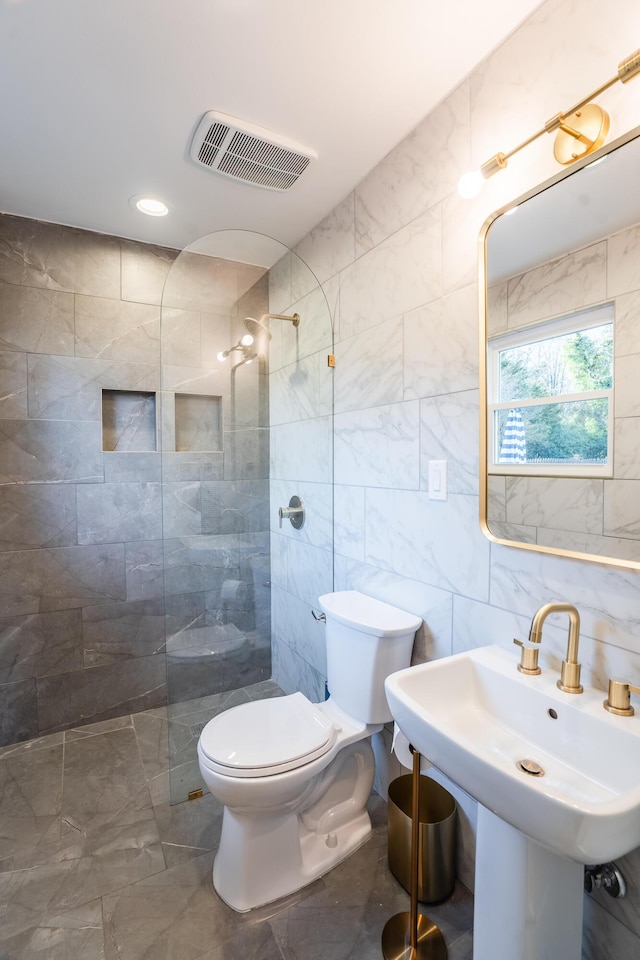 bathroom featuring sink, tiled shower, tile walls, and toilet