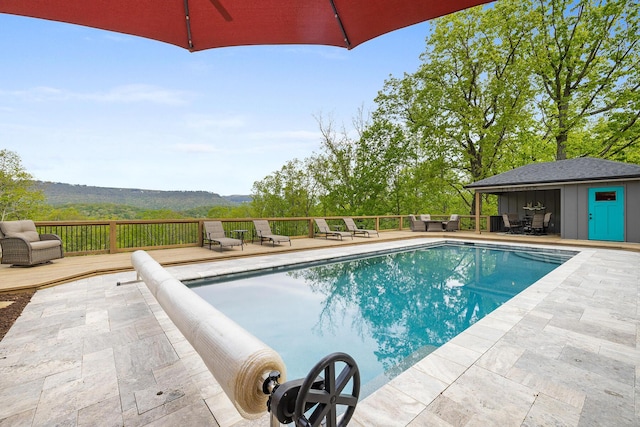 view of swimming pool featuring a deck with mountain view, a patio area, a fenced in pool, and an outdoor structure