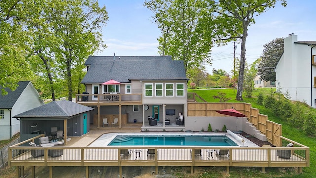 rear view of property with a deck, a shingled roof, a fenced backyard, and a fenced in pool