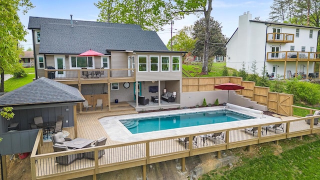 rear view of property with a shingled roof, a fenced backyard, a wooden deck, and a fenced in pool