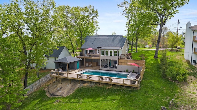 rear view of house with an outdoor pool, fence, a deck, and a yard