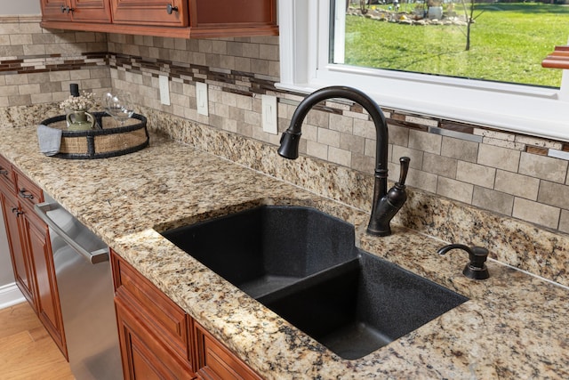 details featuring light wood-style flooring, backsplash, stainless steel dishwasher, a sink, and light stone countertops