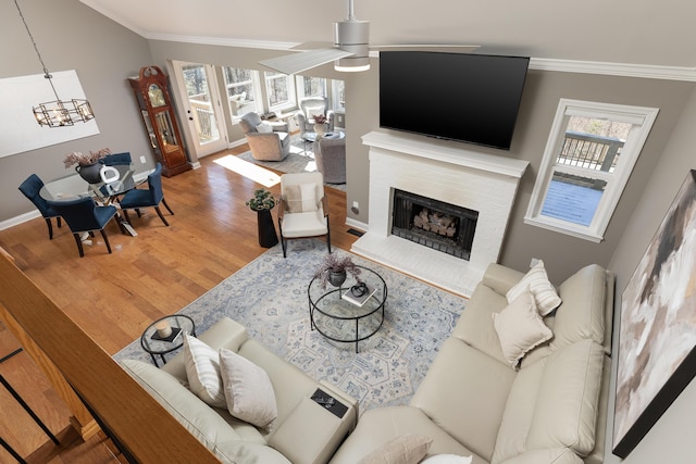 living room with a brick fireplace, plenty of natural light, wood finished floors, and crown molding