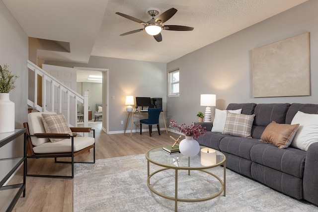 living area with baseboards, ceiling fan, stairs, a textured ceiling, and light wood-style floors