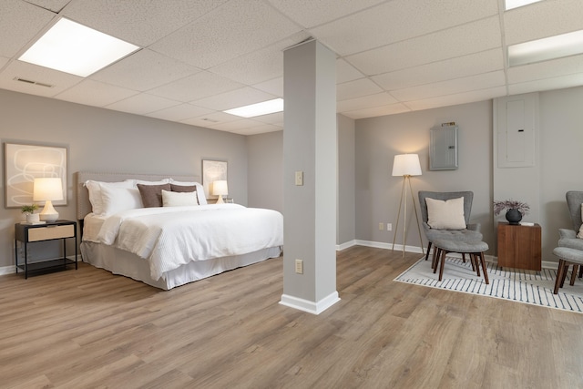 bedroom featuring electric panel, baseboards, visible vents, a drop ceiling, and light wood-style floors