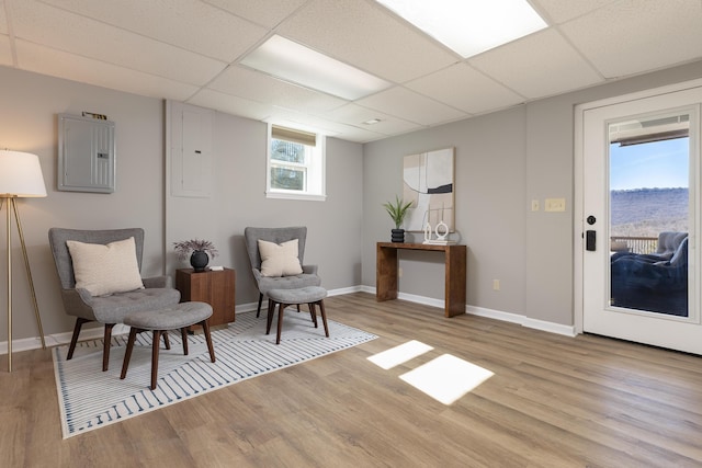 living area featuring light wood-style flooring, a drop ceiling, electric panel, and baseboards